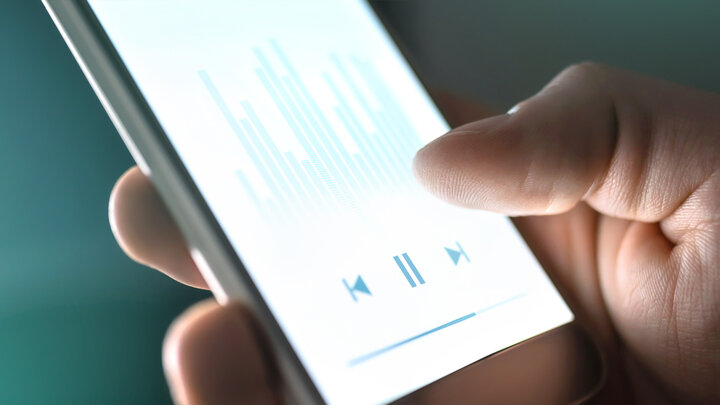 Zdjęcie smartphona trzymanego z dłoni. Na ekranie wyświetlane są symbole odtwarzacza.