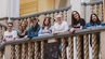 A group of people wearing AGH University merchandise, posing for a photograph, leaning on a staircase railing inside a historic building.