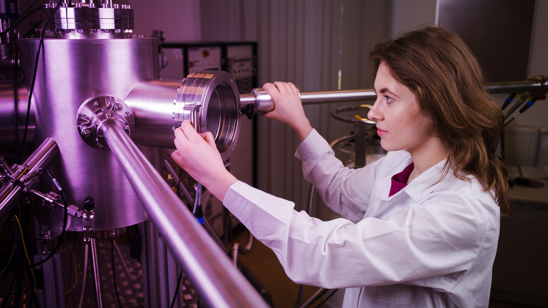 A female scientists with a system of purple-illuminated pipes.