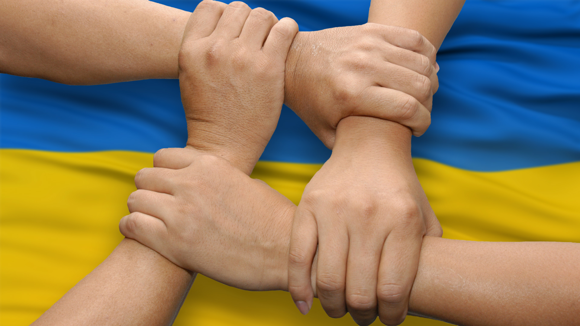 Zdjęcie przedstawia cztery trzymające się wzajemnie ręce na tle żółto-niebieskiej flagi. 