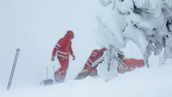 Trzy postacie w czerwonych kombinezonach podczas zamieci śnieżnej