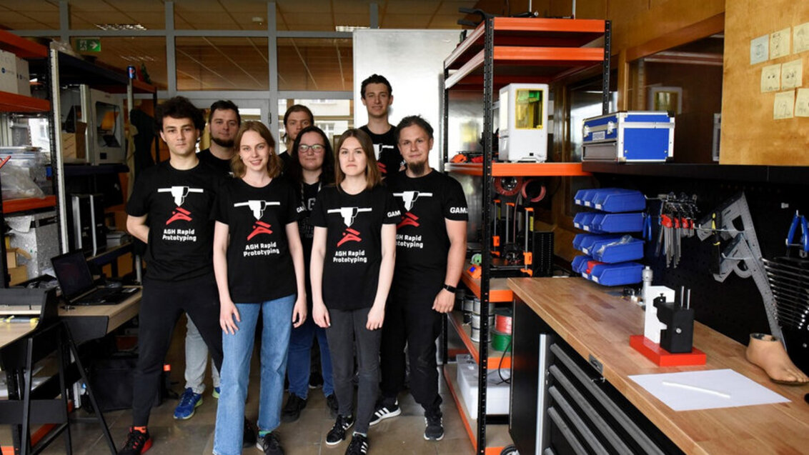 Grupa 8 studentów stojących w laboratorium mechanicznym (z przodu 3 kobiety, a za nimi 5 mężczyzn)