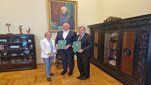 Na zdjęciu troje sygnatariuszy umowy - stoją obok siebie, Rektor AGH i prezes KPT trzymają w dłoniach zielone teczki z podpisanymi dokumentami. Zdjęcie wykonane w gabinecie rektorskim.